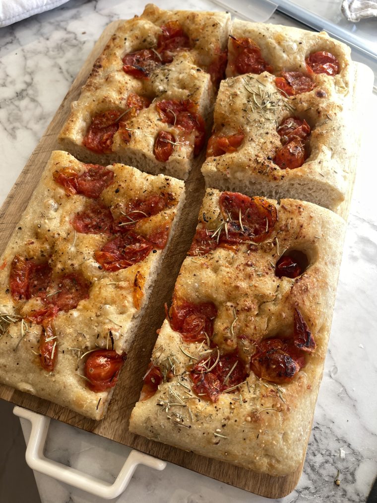 Focaccia na zakwasie z konfitowanymi pomidorkami i rozmarynem pokrojona na kawałki na desce